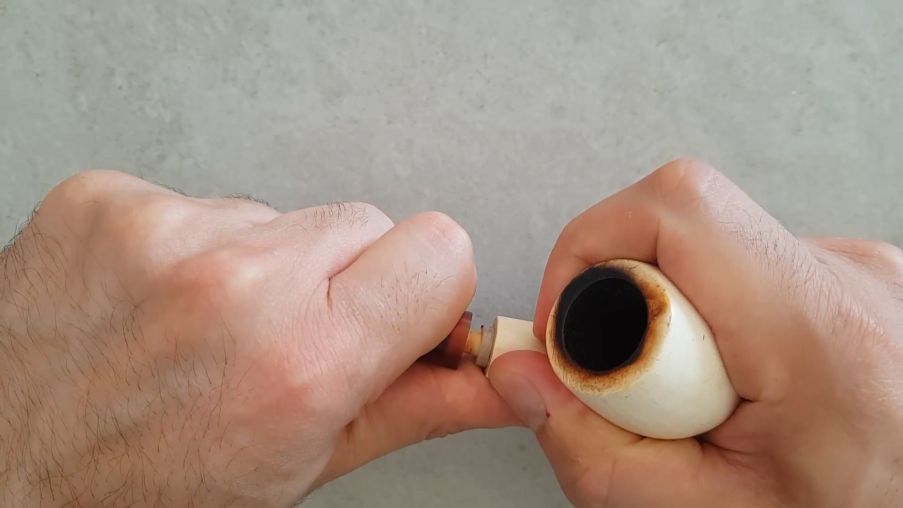 Close-up of hands disassembling a tobacco pipe by gently removing the stem from the bowl, emphasizing that the pipe is cool before handling