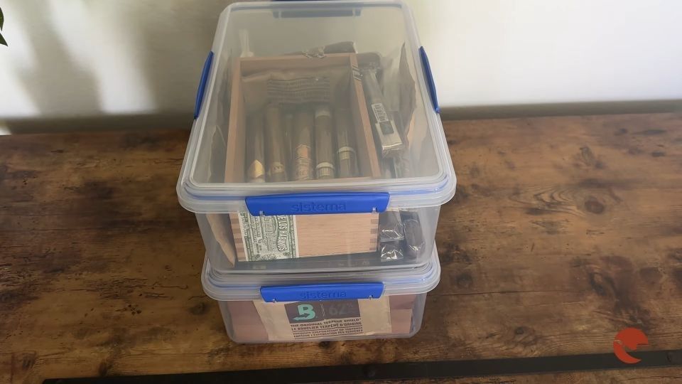 Due contenitori di plastica impilati usati per conservare i sigari con bustine di umidità e scatole di legno con sigari all'interno.