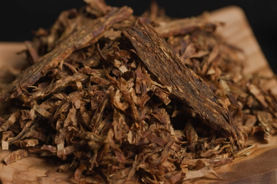 Loose Turkish pipe tobacco with sliced ​​and flake cuts on a wooden surface.