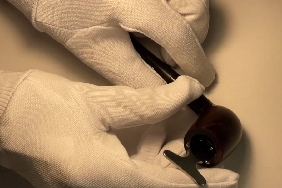 Hands in white gloves trimming carbon build-up inside a tobacco pipe bowl
