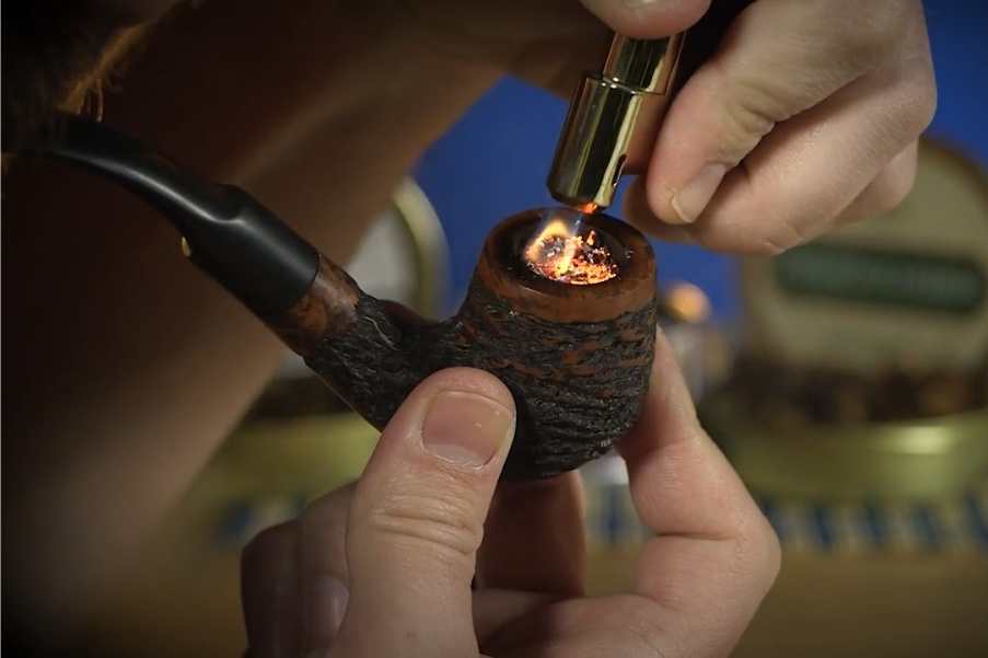 Close-up of a person lighting Turkish tobacco pipe in a rusticated briar pipe with a gold lighter